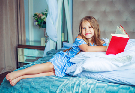 happy little girl reading a book in bed at homeの写真素材