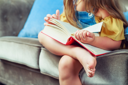 happy little girl reading a book in bed at homeの写真素材
