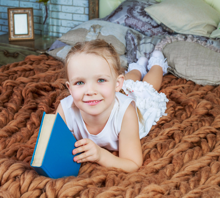 happy little girl reading a book in bed at homeの写真素材