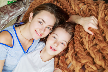 young happy mother and daughter in bed at homeの写真素材