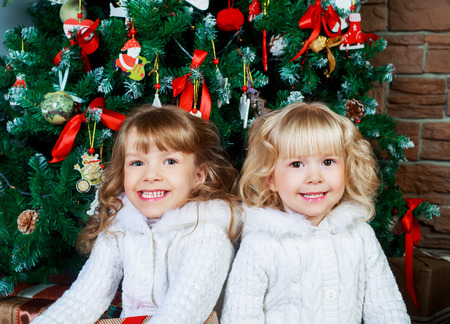 two sisters sitting on the floor at home with Christmas tree and presentsの写真素材
