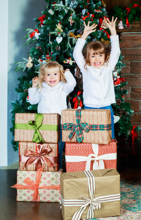 two happy little sisters at home with Christmas tree and presentsの写真素材