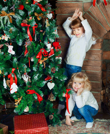 two happy little sisters at home with Christmas tree and presentsの写真素材