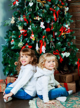 two sisters sitting on the floor at home with Christmas tree and presentsの写真素材