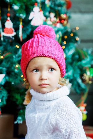 cute little girl wearing a pink hat at home with Christmas treeの写真素材
