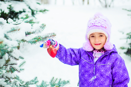 happy little girl decorating  a fir tree in the winter parkの写真素材