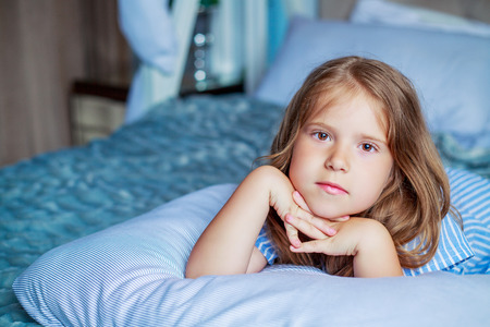 cute little girl with a pillow in bed at homeの写真素材
