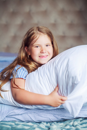 happy little girl with a pillow in bed at homeの写真素材