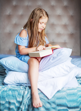 happy little girl with a book and a pillow in bed at homeの写真素材