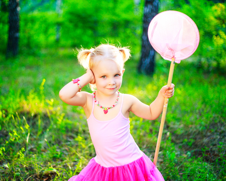 happy little girl wearing a pink dress,  holding a butterfly net, in the summer parkの写真素材