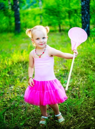 happy little girl wearing a pink dress,  holding a butterfly net, in the summer parkの写真素材