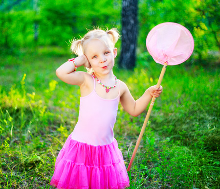 happy little girl wearing a pink dress,  holding a butterfly net, in the summer parkの写真素材