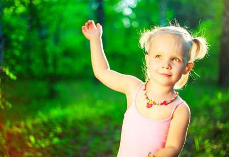 happy little girl wearing a pink dress,  waving her arm, in the summer parkの写真素材