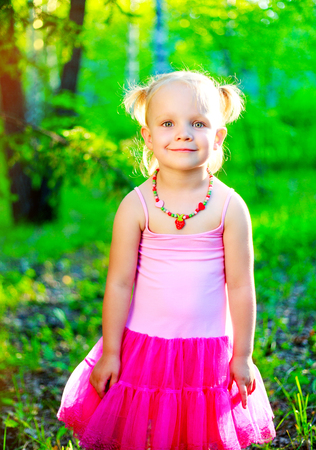 happy little girl wearing a pink dress,  in the summer parkの写真素材