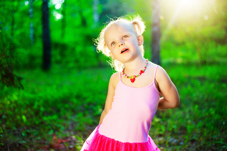 happy little girl wearing a pink dress,  in the summer parkの写真素材