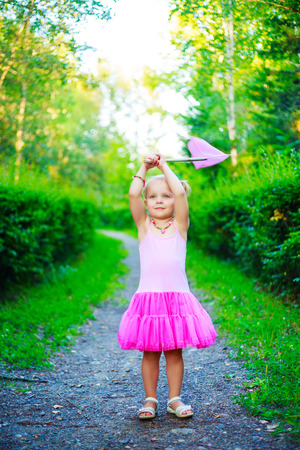 happy little girl wearing a pink dress,  holding a butterfly net, in the summer parkの写真素材