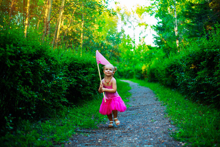 happy little girl wearing a pink dress,  holding a butterfly net, in the summer parkの写真素材