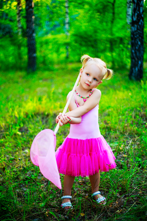 happy little girl wearing a pink dress,  holding a butterfly net, in the summer parkの写真素材