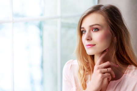 beautiful blond woman with long hair resting at home by the windowの写真素材