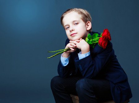 hansome boy wearing a black suit with roses in his hands, isolated against studio backgroundの写真素材
