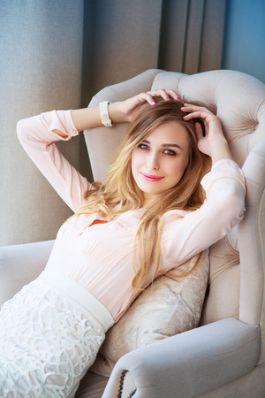 beautiful blond woman with long hair resting at home in the chair by the windowの写真素材