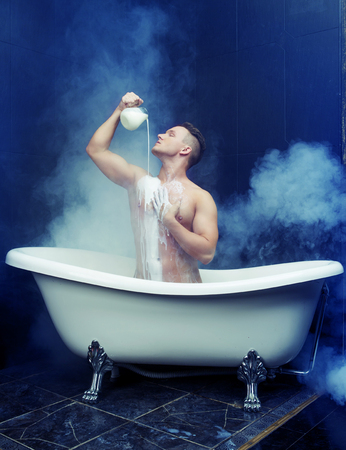 attractive muscular young man taking a bath with milkの写真素材