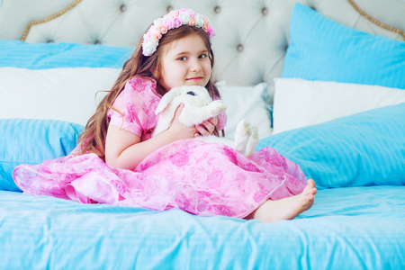 happy little girl with a white rabbit in bed at homeの写真素材
