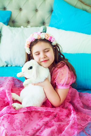 happy little girl with a white rabbit in bed at homeの写真素材