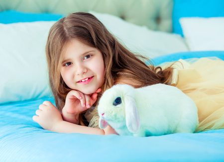 happy little girl with a white rabbit in bed at homeの写真素材