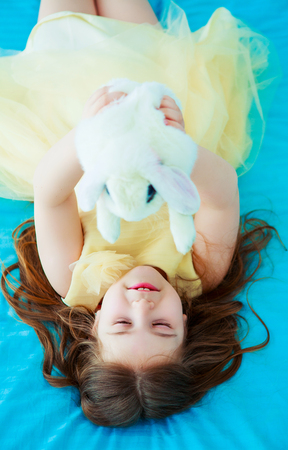 happy little girl with a white rabbit in bed at homeの写真素材