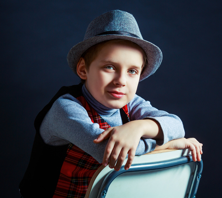 hansome boy wearing a hat and a vest sitting on the chair, isolated against black studio backgroundの写真素材