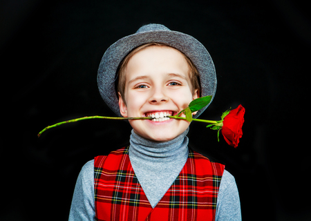 hansome boy wearing a hat and a vest with rose in his teeth, isolated against black studio backgroundの写真素材
