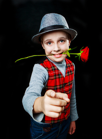 hansome boy wearing a hat and a vest with rose in his teeth, isolated against black studio backgroundの写真素材