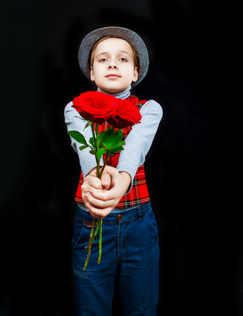 hansome boy wearing a hat and a vest with roses in his hands, isolated against black studio backgroundの写真素材