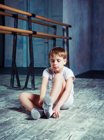 boy ballet dancer putting on pointes at  dance class near the barre indoorsの写真素材
