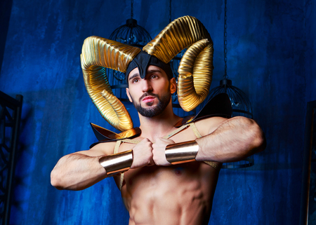 muscular handsome man  wearing a stage costume with big golden horns in the studioの写真素材