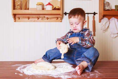 baby at home in the kitchen with dough and flour on the tableの写真素材