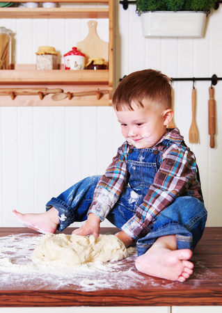 baby at home in the kitchen with dough and flour on the tableの写真素材