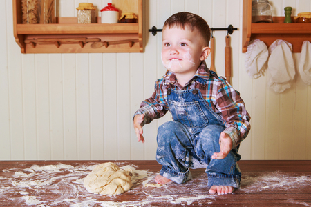 baby at home in the kitchen with dough and flour on the tableの写真素材