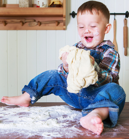 baby at home in the kitchen with dough and flour on the tableの写真素材