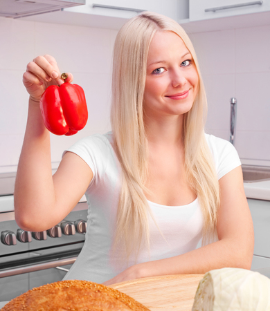 beautiful young blond woman eating peppers at home in the kitchenの写真素材