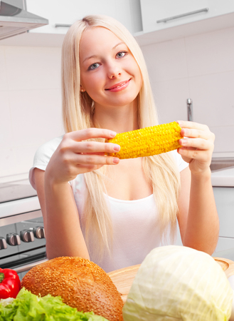 beautiful young blond woman eating vegetables at home in the kitchenの写真素材