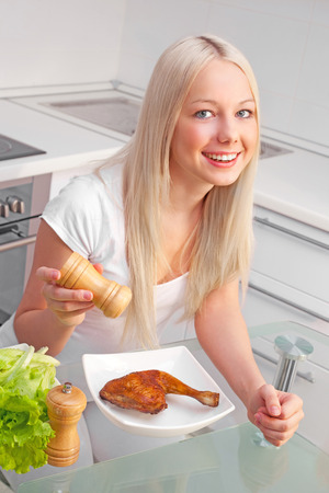 beautiful young blond woman eating fried chicken at home in the kitchenの写真素材