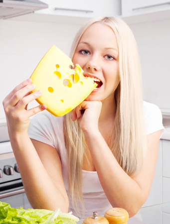 beautiful young blond woman eating cheese at home in the kitchenの写真素材