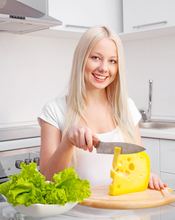 beautiful young blond woman eating cheese at home in the kitchenの写真素材