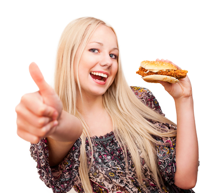 beautiful young blond woman with a burger and her thumb up, isolated against white backgroundの写真素材