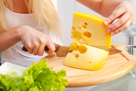 hands of a young woman eating cheese at home in the kitchenの写真素材
