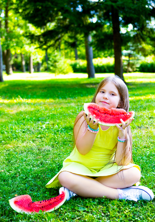 happy little girl eating watermelon outdoor in the summer parkの写真素材