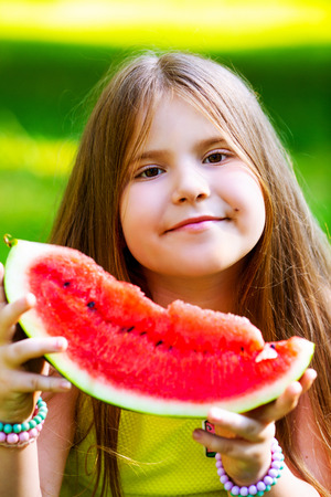 happy little girl eating watermelon outdoor in the summer parkの写真素材