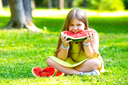 happy little girl eating watermelon outdoor in the summer parkの写真素材